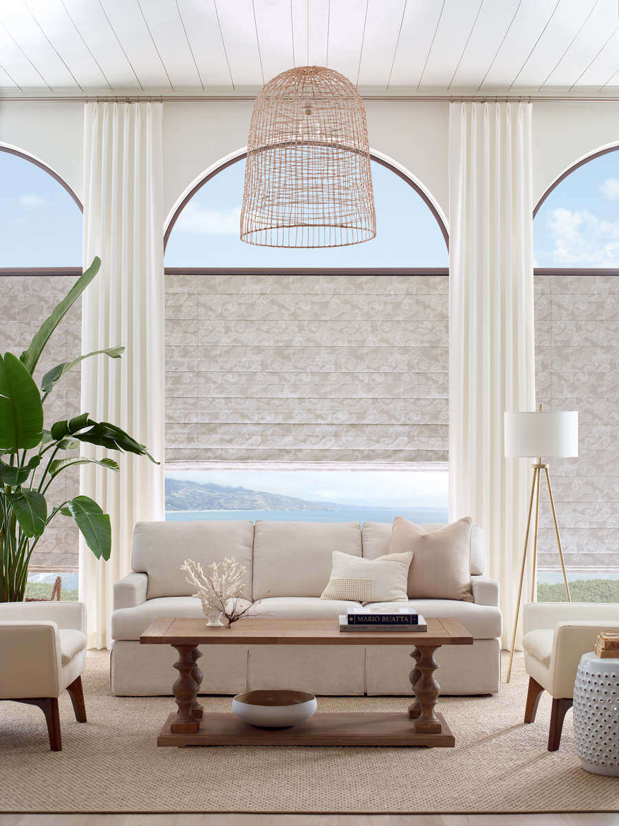 contemporary coastal living room with large arched windows roman shades and designer drapery in neutral tones