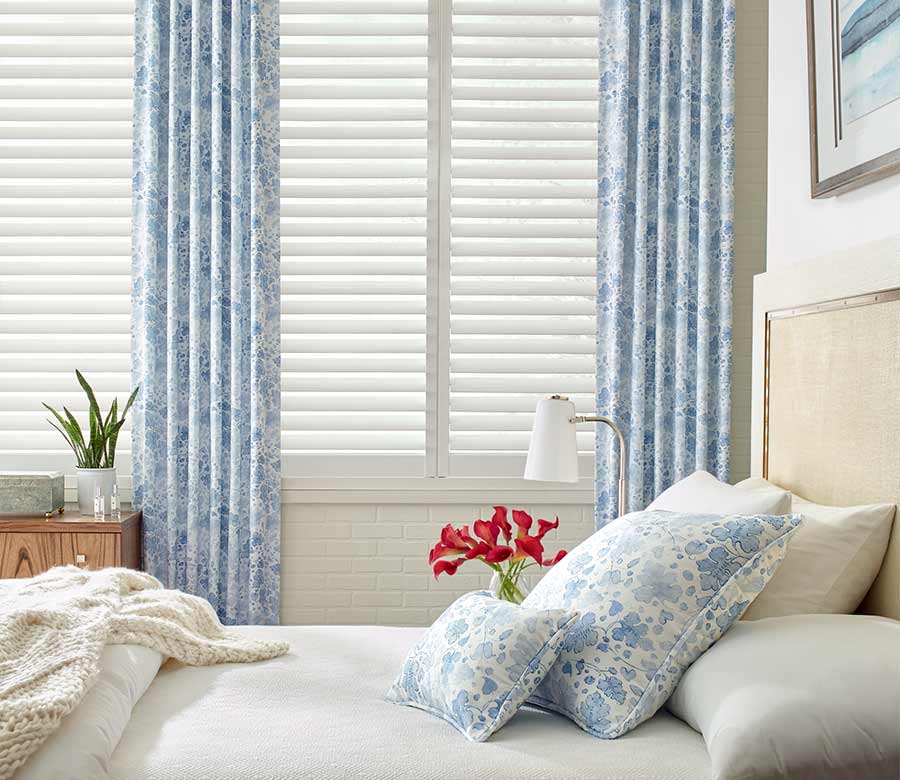 coastal guest bedroom white plantation shutters framed by blue floral curtains in reno, NV