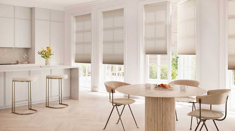 Duette® Honeycomb Shades covering floor to ceiling windows in a neutral kitchen. To the right of the photo is two chairs and a modern circular table 